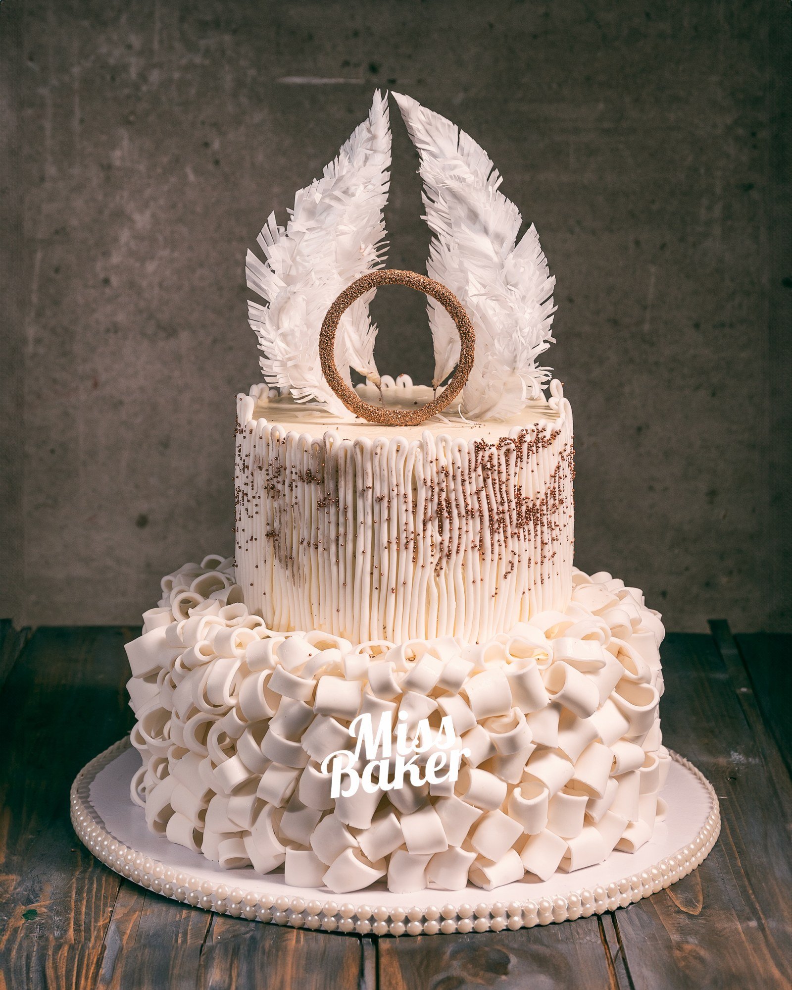Torturi de nuntă de la Miss Baker — pene albe sculptate, inel decorativ central, volane ample